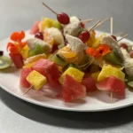 Fruit skewers with watermelon, pineapple, kiwi, and grapes on a white plate