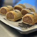 Close-up of golden puff pastry sausage rolls on baking tray
