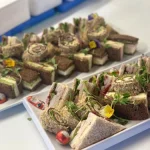Platter of triangle-cut gourmet sandwiches with mixed fillings, ideal for catering lunches, events, or finger food menus