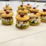 Gourmet mini sandwich stacks with fillings and grape garnish, ideal for wedding catering, brunch menus, or corporate finger food