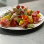 Assorted fruit skewers with edible flowers on a plate for catering